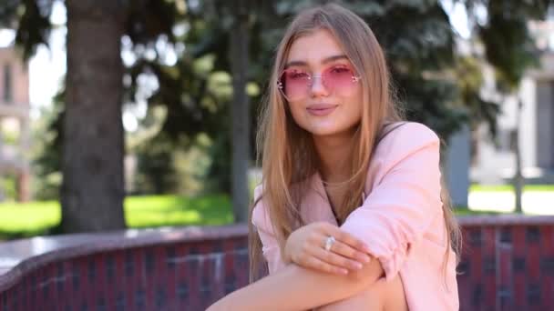 Adorável adolescente com cabelo loiro longo em linha reta sentado no parque — Vídeo de Stock