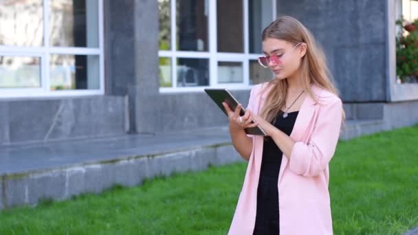 Ung blondin arbetar på TabletPC i city. Kvinna med trådlöst internet på gatan. Mobil kommunikation-konceptet. — Stockvideo