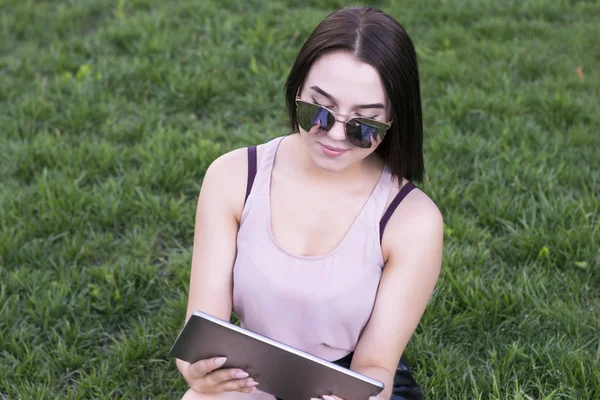 Çayır üzerinde oturan ve tablet tarama muhteşem bir kadın