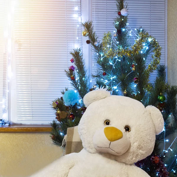 Украшенная елка и большой плюшевый мишка. Симпатичный новогодний подарок под сияющей сосной — стоковое фото
