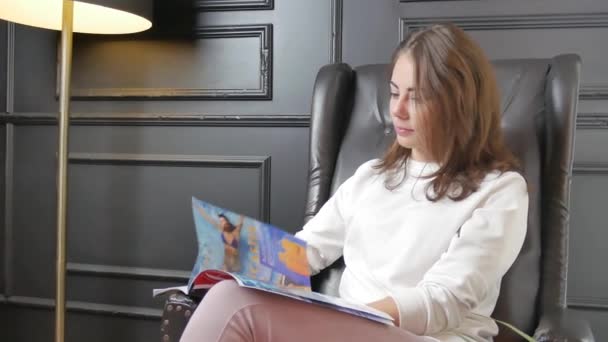 Chica sentada en la silla y leyendo revista — Vídeos de Stock