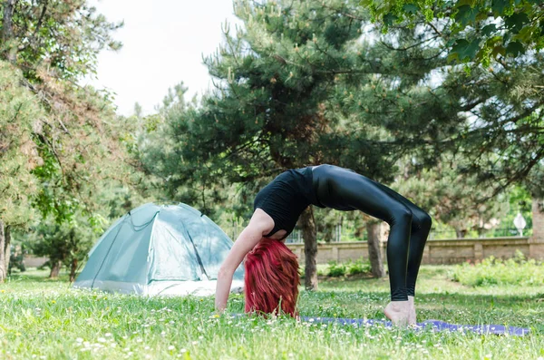 Woman doing morning yoga exercises in woods near yellow tourist