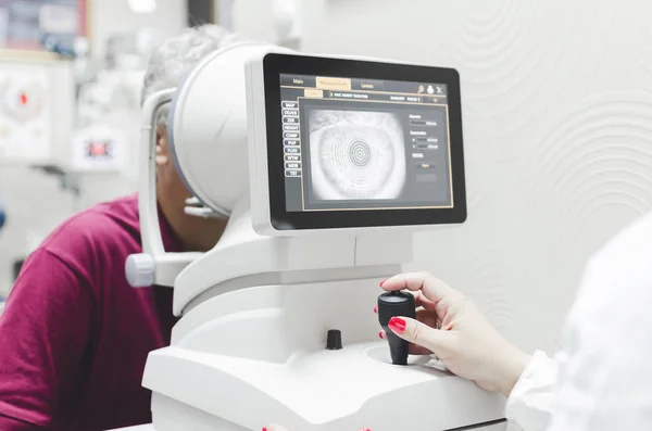 health care, medicine, people, eyesight and technology concept - close up of optometrist with autorefractor checking patient vision at eye clinic or optics store