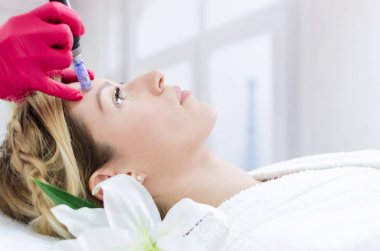 Hardware cosmetology, mesotherapy, portrait of young woman getting treatment of forehead zone at spa. clipart