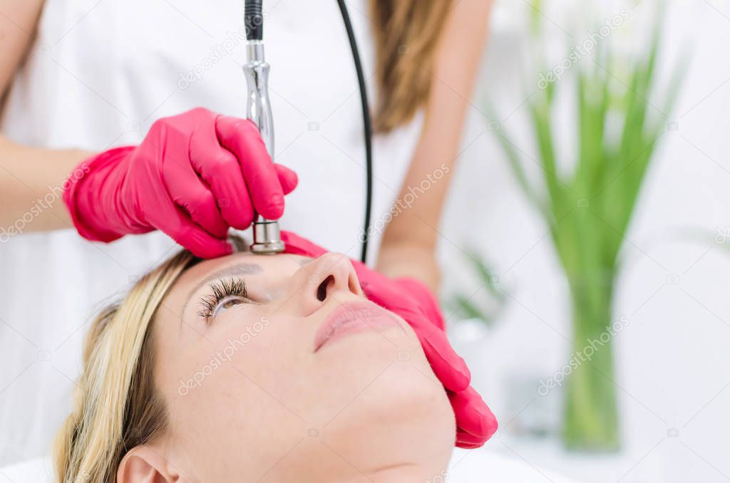 Close up of cosmetologist who makes the procedure microdermabrasion of the facial skin of a beautiful, young woman in a beauty spa salon.