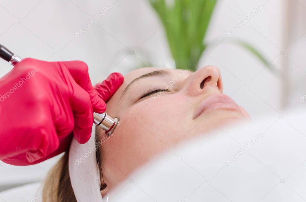 Close up of cosmetologist who makes the procedure Microdermabrasion of the facial skin of a beautiful, young woman in a beauty salon.