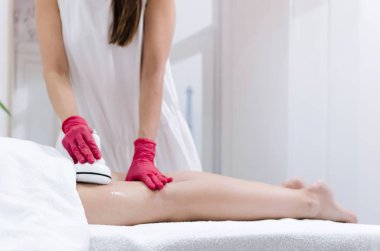 Young woman receiving radiofrequency lifting massage of her legs at beauty spa salon. clipart