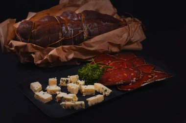 Close up of sliced dried meat and cheese on plate on black background clipart