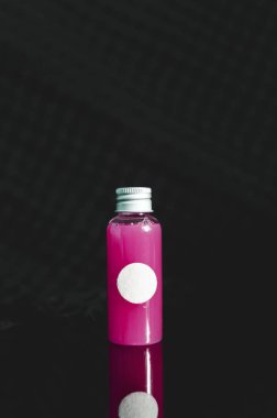 küçük dolu cam şişe pembe sıvı ve beyaz boşluk ile siyah arka plan, tıp kavramı üzerine önden görünüm
