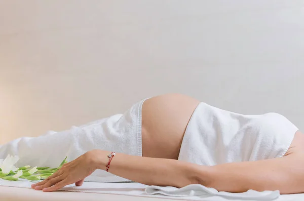 Cropped photo of pregnant woman in wellness spa salon, lying on spa table and relaxing. Space for text.