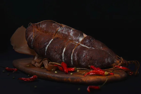 close up of piece of smoked meat, pepperoni and pepper on wooden table