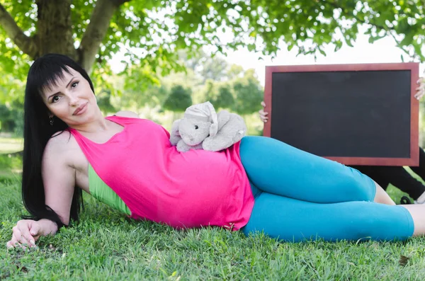 Красивая Беременная Женщина Лежит Парке Дочерью Которая Держит Пустую Доску — стоковое фото