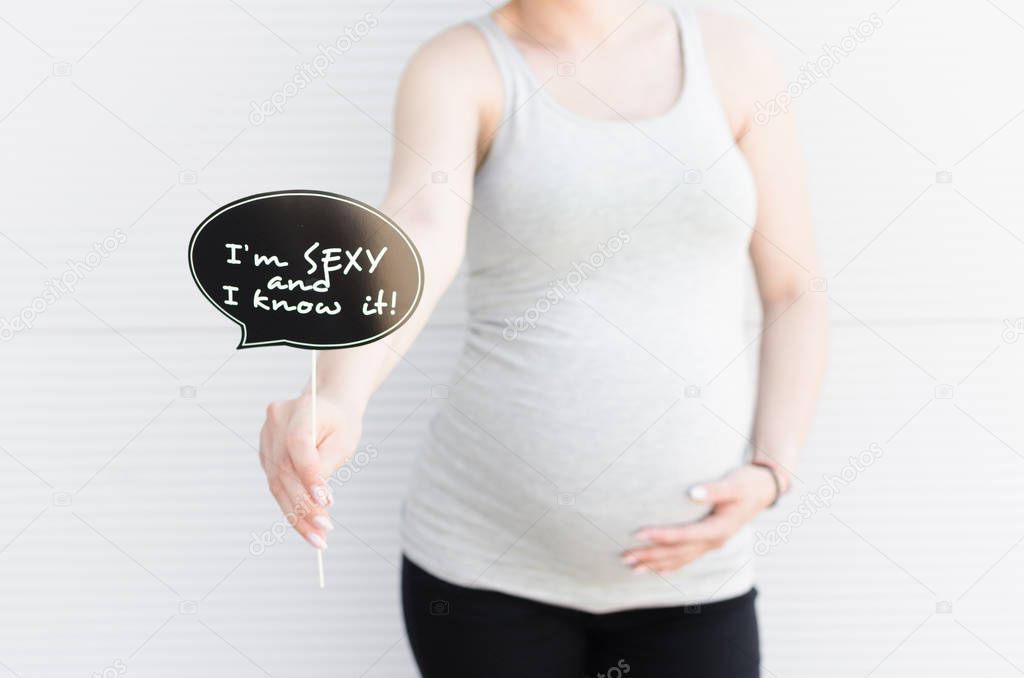 Cropped image of pregnant woman holding a photo booth prop with a funny quote.