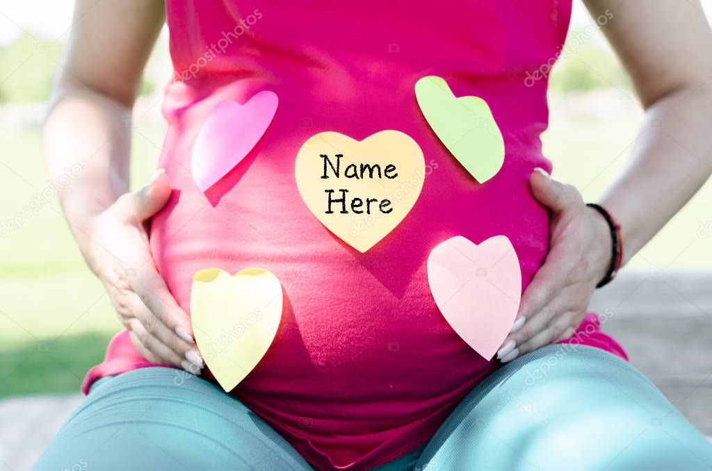 Torso of a pregnant woman having sticky notes on her belly preparing to find a name for the baby.