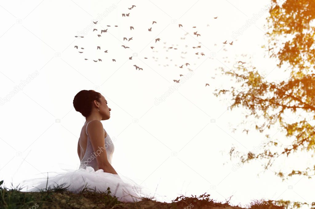 Portrait of young beautiful ballet dancer sitting in nature, on top of a cliff.