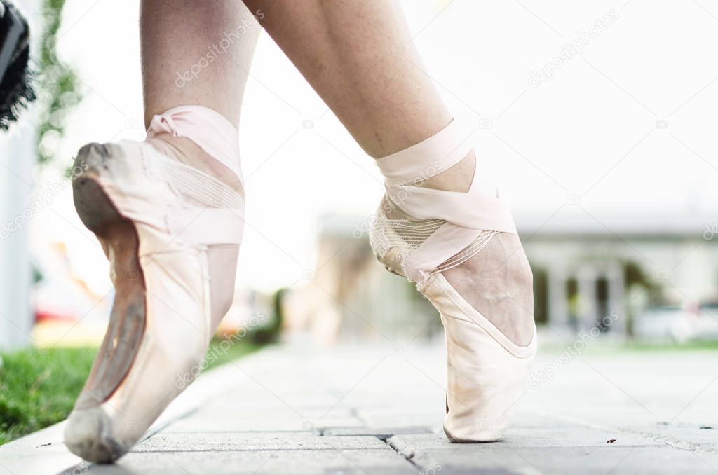 Close up of feet of female ballet dancer in pointe shoes, posing on street.