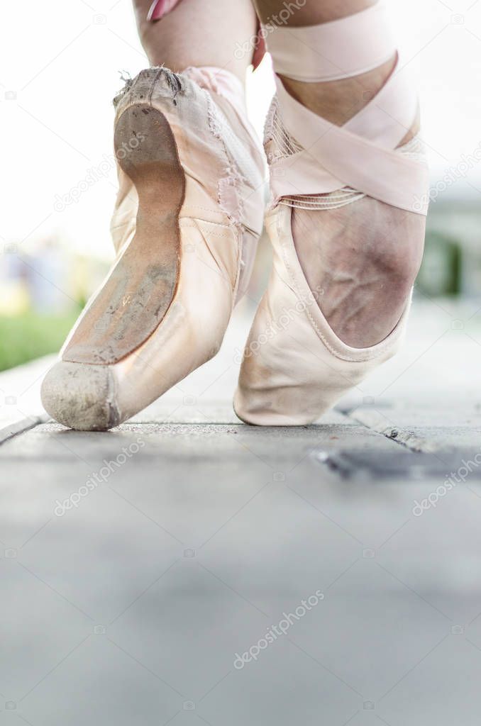 Vertical image of feet of young ballerina, posing on the street in pointe shoes, space for text.