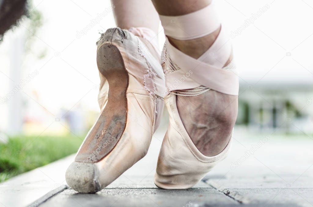 Close up of feet of young female classic ballet dancer in pointe shoes, posing in nature.