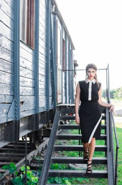 Genç güzel kadın modeli önden görünümü içinde siyah eski trenin önüne poz giyinmiş.