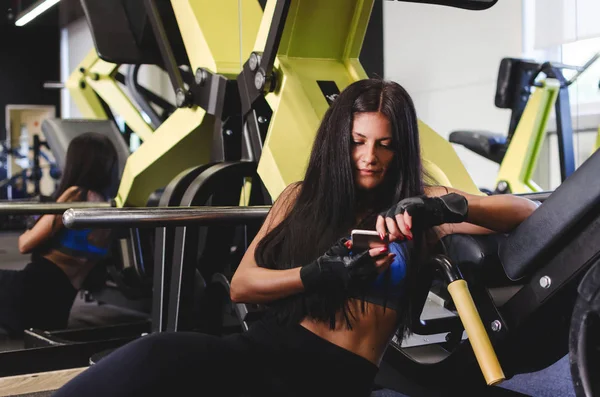 Young woman sitting on floor in a gym taking a break on her smartphone.