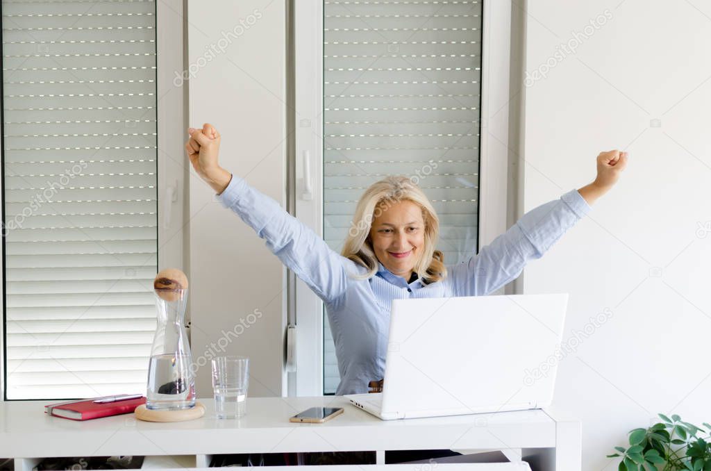 Portrait of senior  woman with hands up working at home on laptop, space for text.