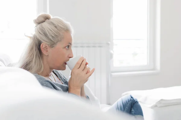 カップから飲むと リビングのソファーに座っている年配の女性の肖像画 テキストのためのスペース — ストック写真