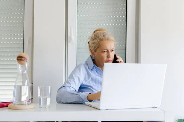 Portrait of senior woman working at home on laptop.