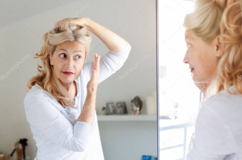 Senior beautiful woman checking her hair in front of mirror at home.