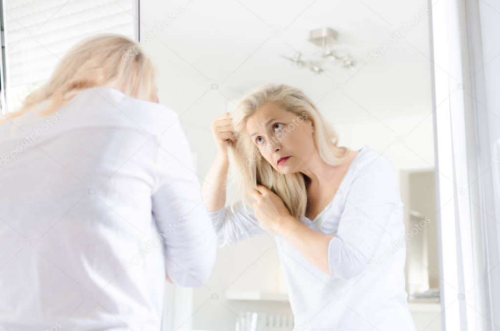 Senior beautiful woman standing in front of mirror looking in her hair.