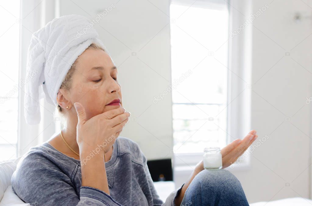 Senior woman putting cream on face at home.