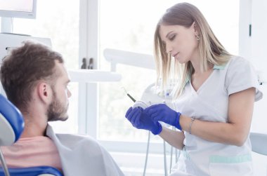 Erkek hastaya diş beyazlatma için hazırlık yaparken genç kadın dişçi portresi.