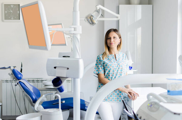 Portrait of beautiful young female dentist in office. Equimpent in background.