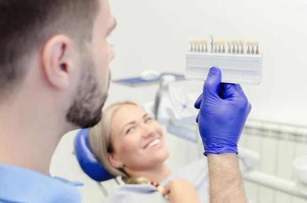 メスの患者に歯を白くする前に色のサンプルを見て男性歯科医 — ストック写真