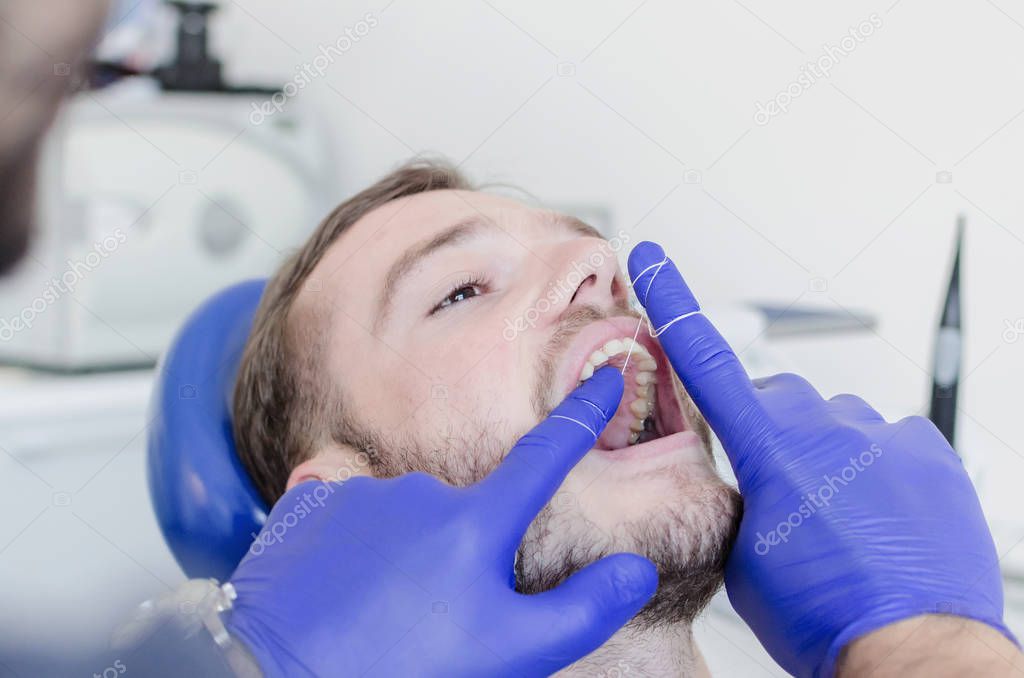 close up of male patient with mouth open having teeth cleaning with thread at dentist.