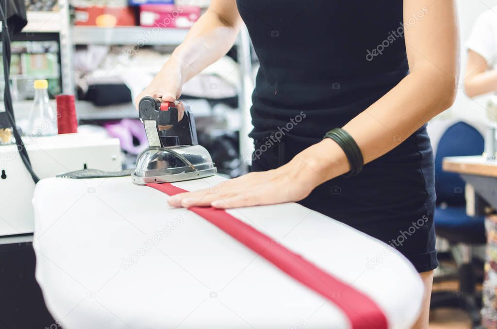 Tailor stroking fabric with steam iron in workshop