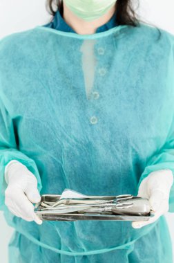 Bir kadın dişçi steril diş araçları ile tepsi tutarak resim kırpılmış.