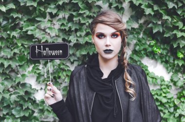 Kameraya bakarak ve fotoğraf-çizme prop Halloween metinle elinde tutan genç kadın.