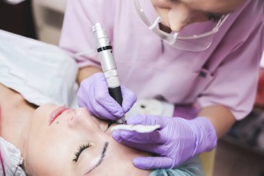 Güzellik salonu bulunan genç bayan hasta, kalıcı makyaj yaparken profesyonel güzellik uzmanı, yakın çekim