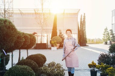 Genç kadın bahçıvan kürek tutan ve botanik bahçe içinde güzel güneşli bir günde ayakta önlük ile