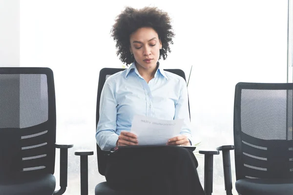 young business woman sitting on chair in waiting room with papers before meeting with potential business partners