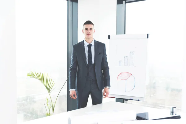 Front view of smart ambitious young manager standing in his office and looking at camera