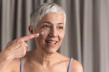 Anti yaş krem yüz koyarak onun gece Cilt Bakımı Rutin yapıyor kısa gri saçlı güzel kadın kıdemli