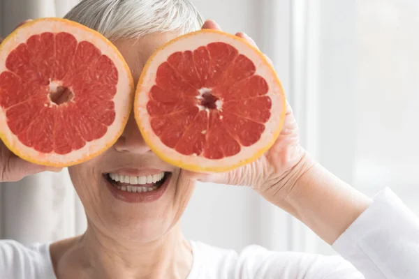 senior woman with young spirit posing with grapefruit and smiling, healthy nutrition and energy concept