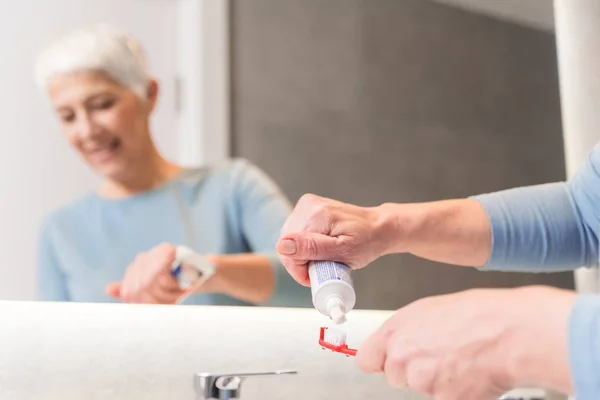 senior woman putting tooth paste on toothbrush in her bathroom