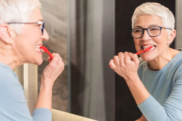 Schöne Seniorin Die Ihre Zähne Wäscht Und Ihr Spiegelbild Spiegel — Stockfoto