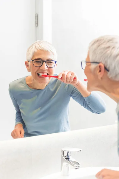 Schöne Seniorin Die Ihre Zähne Wäscht Und Ihr Spiegelbild Spiegel — Stockfoto