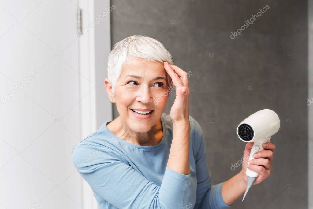 senior woman with gorgeous smile and glowing skin drying her short gray hair at home
