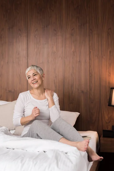Beautiful senior woman waking up with neck pain and stretching in her bedroom