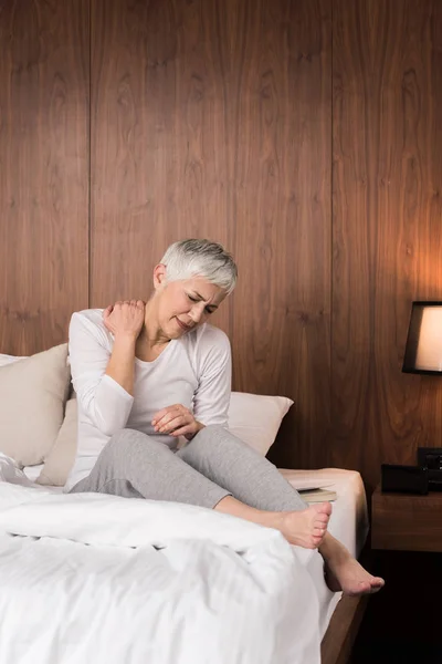 Stressed mature woman touching her painful back and feeling discomfort in her bedroom