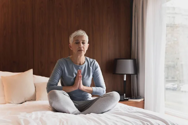 Beautiful senior woman meditating in her bedroom